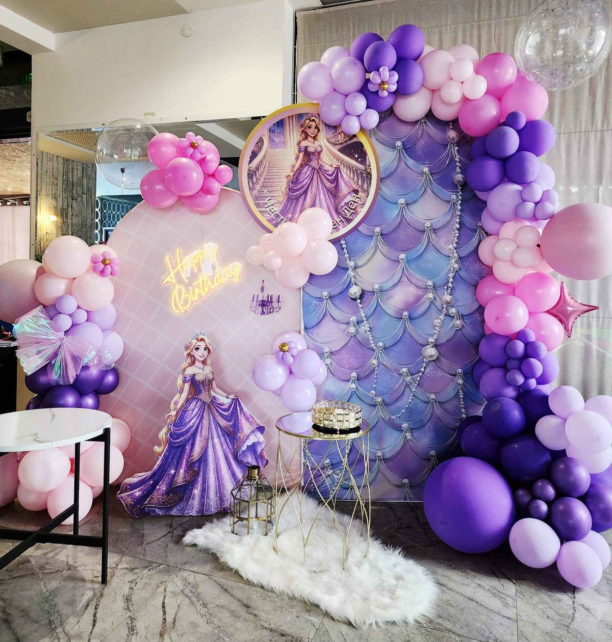 Themed balloon decor for a girl's birthday: an organic garland in pink, blush, lavender and purple around two backdrops, a Happy Birthday neon sign and a cake table